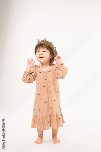 Cute little girl in beige dress with gold crown isolated on white background. Portrait of happy little girl.