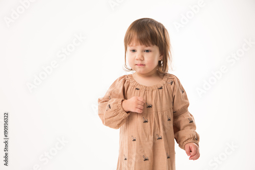 Cute little girl in beige dress isolated on white background. Portrait of happy little girl on white background. Sweet girl with curly hair.