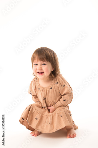 Cute little girl in beige dress isolated on white background. Portrait of happy little girl on white background. Sweet girl with curly hair.
