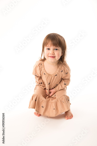 Cute little girl in beige dress isolated on white background. Portrait of happy little girl on white background. Sweet girl with curly hair.