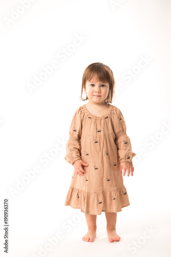 Cute little girl in beige dress isolated on white background. Portrait of happy little girl on white background. Sweet girl with curly hair.