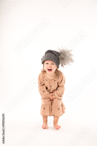 Portrait of happy little girl. Cute little girl in beige dress in a gray hat isolated on white background.