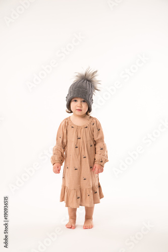 Portrait of happy little girl. Cute little girl in beige dress in a gray hat isolated on white background.