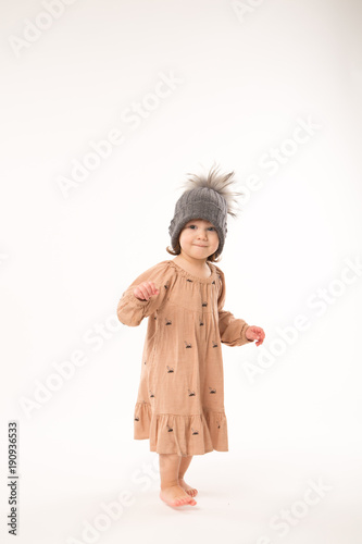 Portrait of happy little girl. Cute little girl in beige dress in a gray hat isolated on white background.