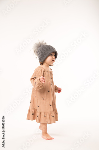 Portrait of happy little girl. Cute little girl in beige dress in a gray hat isolated on white background.