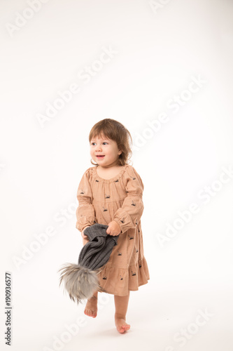Portrait of happy little girl. Cute little girl in beige dress in a gray hat isolated on white background.