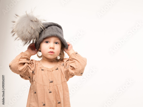 Portrait of pensive little girl. Cute little girl in beige dress in a gray hat isolated on white background.