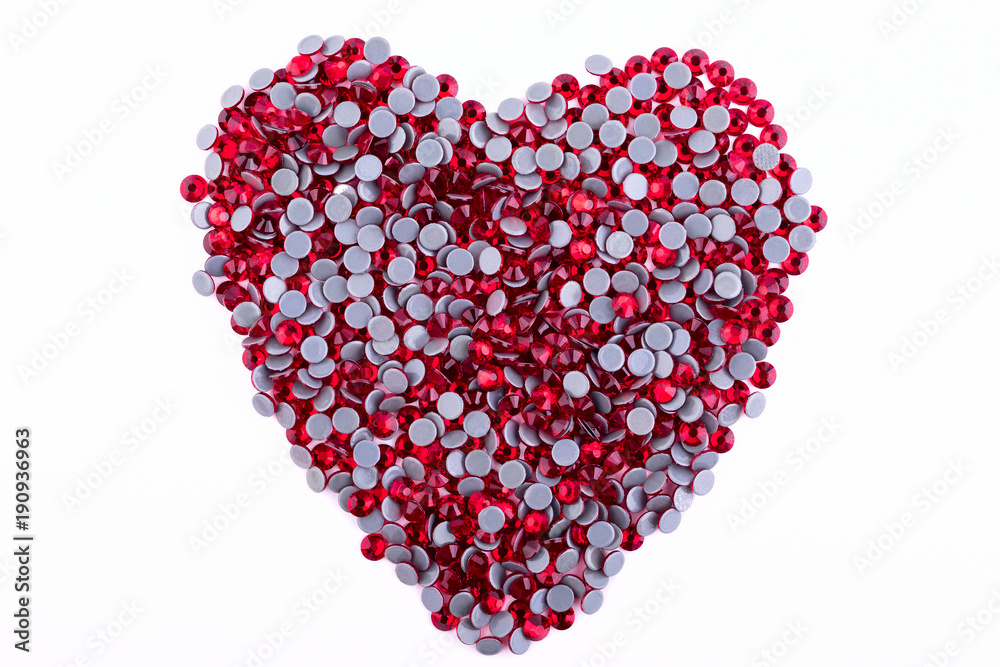 A lot of red rhinestones made in the shape of a heart on a white background. Top view. A lot of red rhinestones made in the shape of a heart on a white background. Top view.
