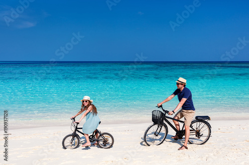 Father and daughter riding bikes at tropical beach