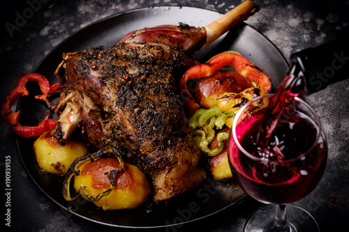Roasted lamb shank with spices and grilled vegetables and red wine glass poured with wine