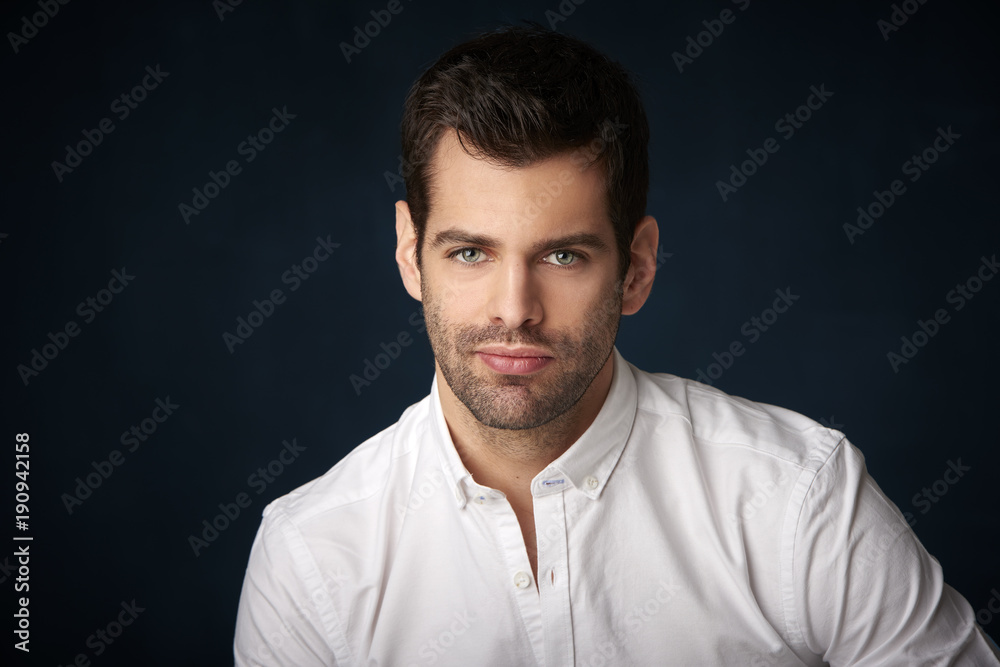 Fototapeta premium Thinking young businessman portrait. Studio portrait of handsome man wearing shirt while sitting at dark background and looking at camera