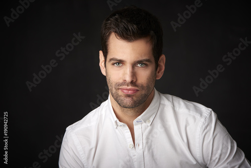 Handsome young man studio portrait. Studio portrait of confident young businessman wearing shirt and looking at camera whle standing at dark background with copy space.