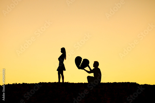 Man begging a woman for love by giving a big broken heart in sunset silhouette background / Disappointed love concept photo