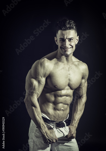 Good Looking Young Gym Fit Man Showing His Sexy Six Pack Abs While Looking at the Camera. Isolated on Black Background.