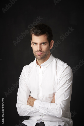Thinking young businessman portrait. Studio portrait of handsome man wearing shirt while sitting at dark background and looking at camera