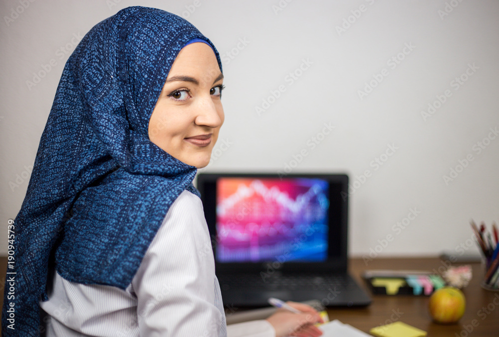 Covered young Muslim with hijab, in office, business and finance, laptop on office desk, economy, accounting Covered young Muslim with hijab, in office, business and finance, laptop on office desk, economy, accounting