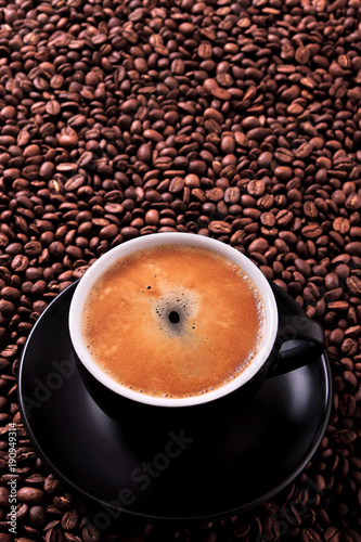 Black coffee cup and saucer one single for espresso or capuccino filled full of coffee beans on a background of scattered dark coffee beans photo vertical