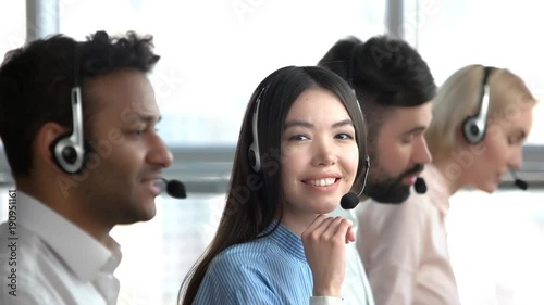 Asian girl in call center flirting. Asian tech support worker cheerfully smiling. Young asian girl turning head. photo