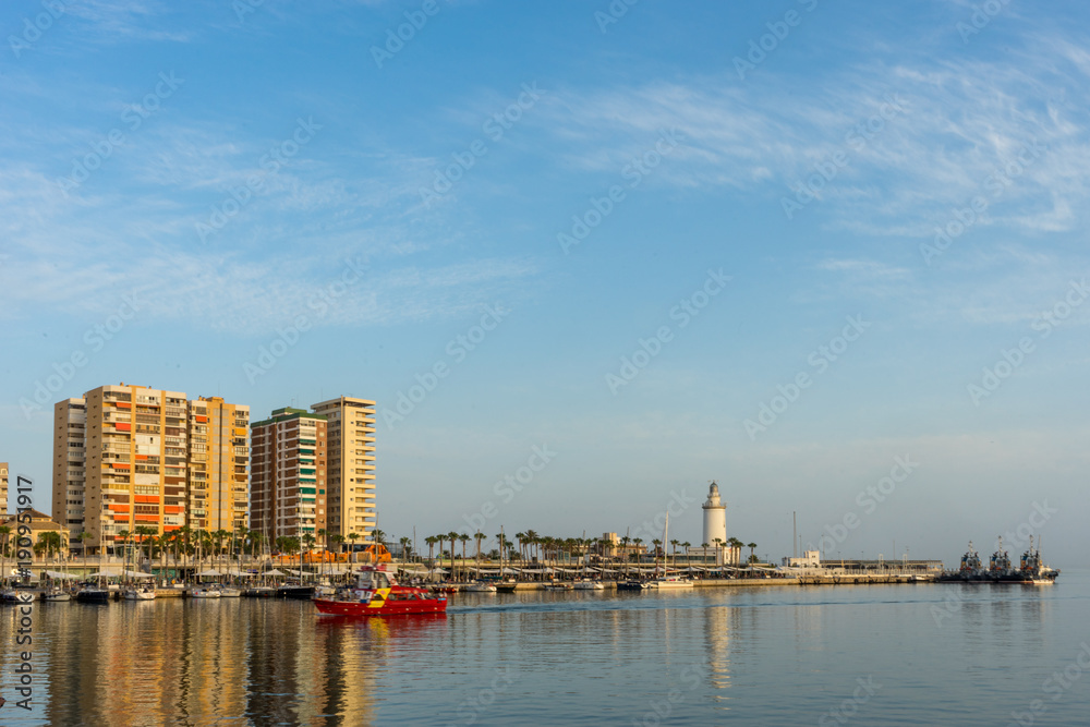 White lighthouse and the tall buildings of Malaga with their reflections in Malaga, Spain, Europe