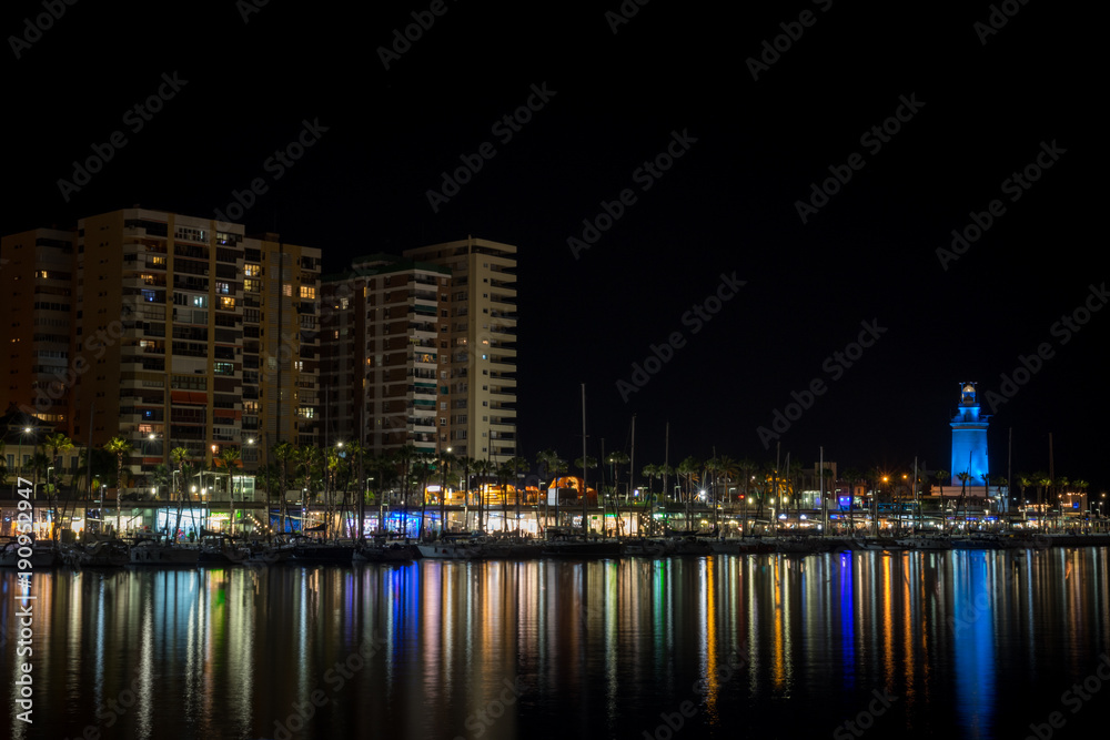 View of Malaga city and lighthouse and their reflections on water from harbour, Malaga, spain, Euope at night