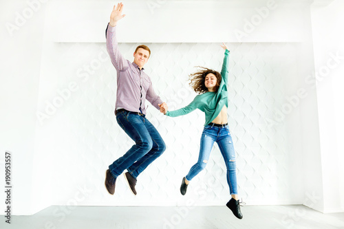 Fototapeta Naklejka Na Ścianę i Meble -  boyfriend and girlfriend jumping holding hands against a background of a decorated white wall