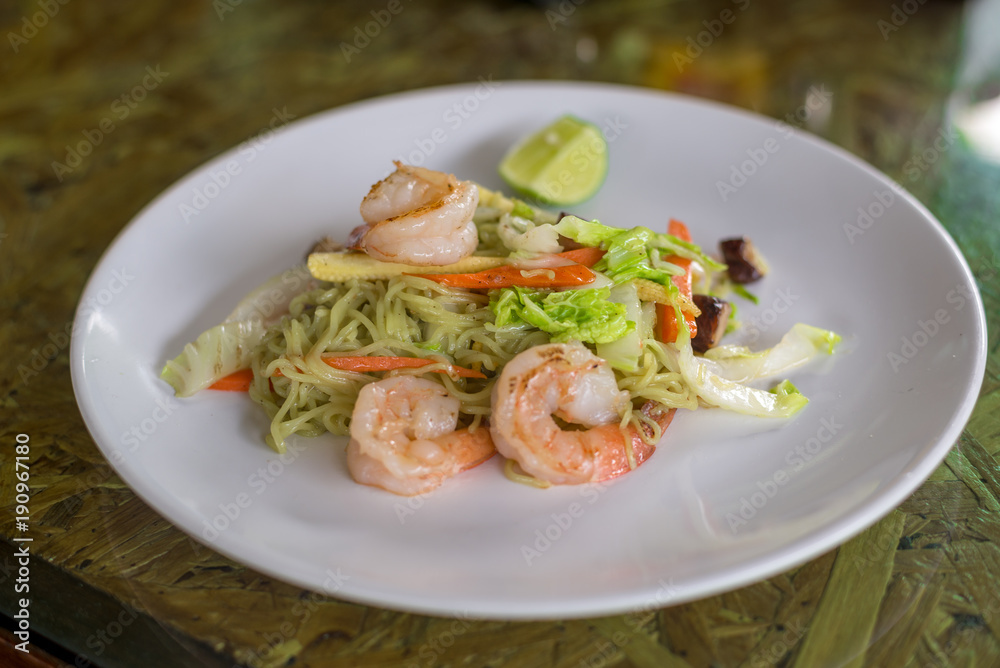 Green Noodle stir fired with shrimp, lettuce, corn and carrot in white plate on wooden table, Thai food