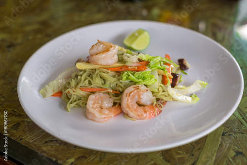 Green Noodle stir fired with shrimp, lettuce, corn and carrot in white plate on wooden table, Thai food