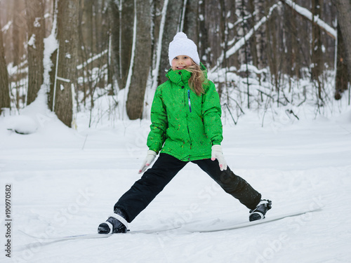 Girl in overalls performs stretching exercises on skis.