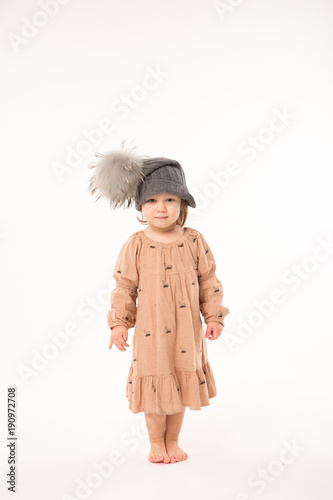 Portrait of happy little girl. Cute little girl in beige dress in a gray hat isolated on white background.