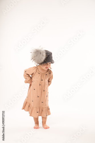 Portrait of happy little girl. Cute little girl in beige dress in a gray hat isolated on white background.
