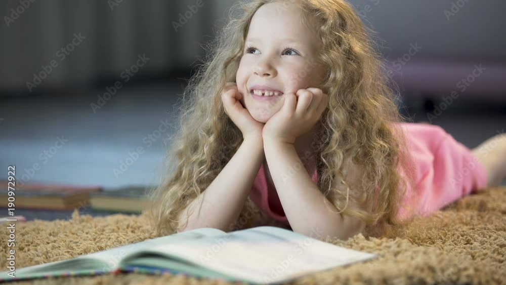 Cute young girl dreaming about happy future, lying on soft carpet at home