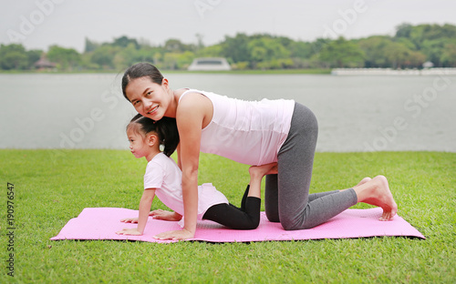 Pregnant mother and her daughter doing yoga in the public park.