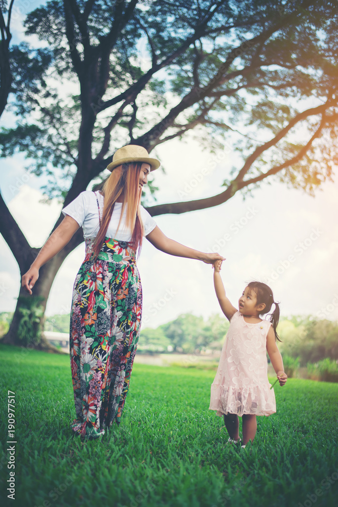 Young mother and her little daughter walking in ther park