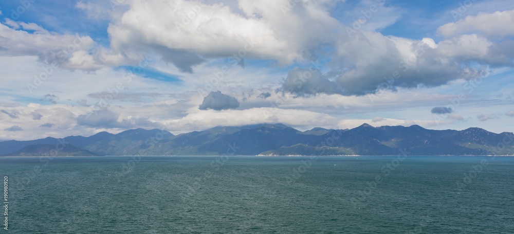 Ocean waves lapping across the south china sea in central Vietnam with a mountain range and cloudy dramatic skies.