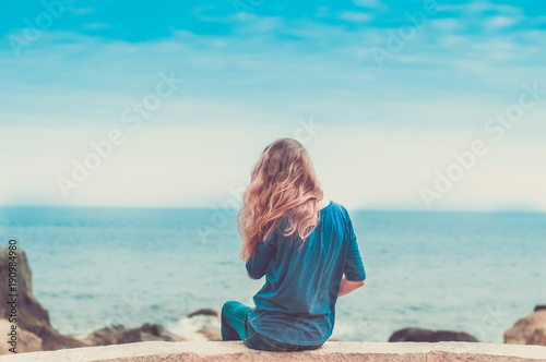 One girl with long blond hair sits by the sea. Toned image © Iryna