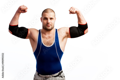 Young athletic man in blue tights and black elbow stands and shows biceps on white isolated background