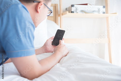 Young asian man touching on mobile phone screen in bedroom