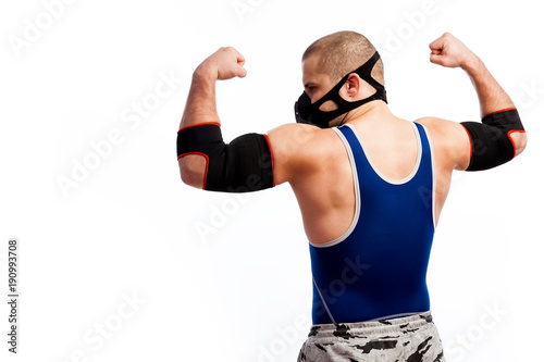 Young sporty man in blue tights, black training mask and black elbow pads is standing with his back and showing biceps on white isolated background © Виталий Сова