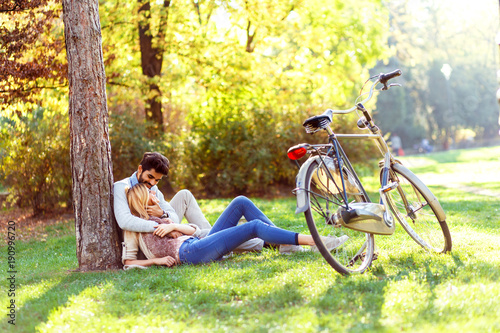 Young couple in love sitting in a autumn park leaning against a tree embracing one another.