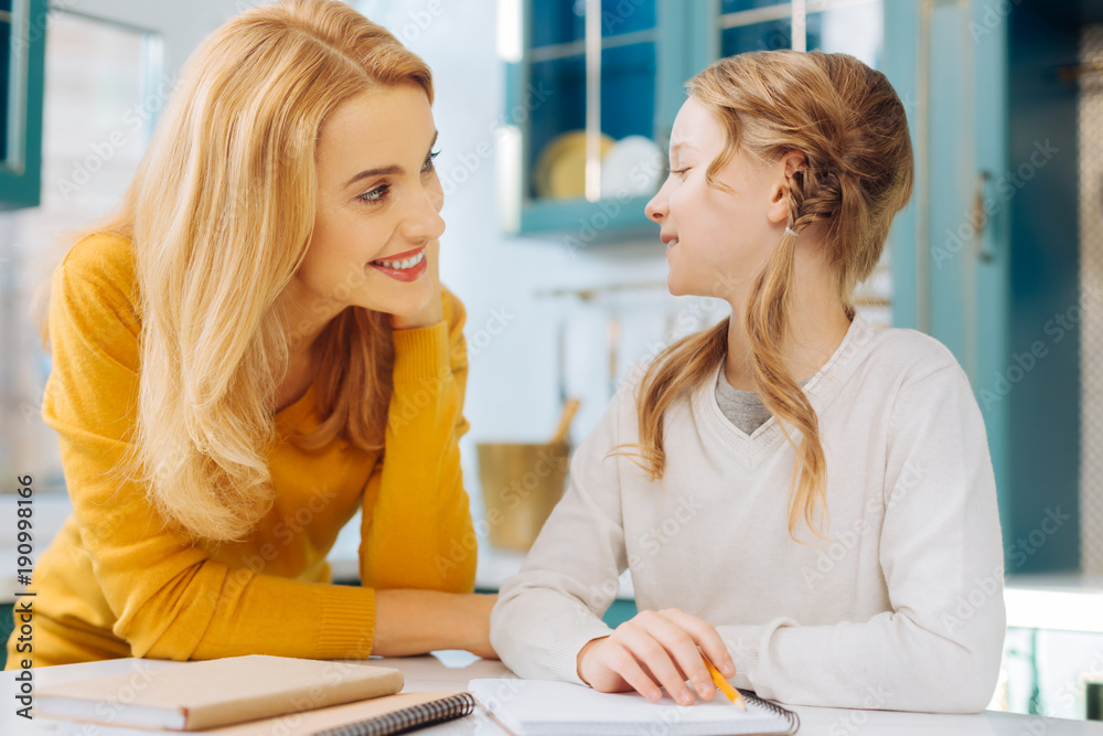 Best mom ever. Attractive joyful fair-haired girl smiling and holding a pencil while she and her mother looking at each other Best mom ever. Attractive joyful fair-haired girl smiling and holding a pencil while she and her mother looking at each other