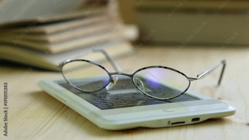 E-book and glasses on the background of paper books. E-book and glasses on the background of paper books.