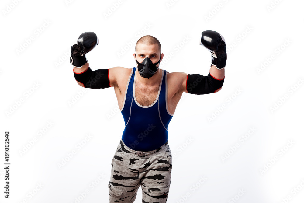 Young sportive man in blue tights,black elbow, black and white boxing gloves   and training mask  stands and show biceps on a white isolated background