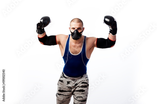 Young sportive man in blue tights,black elbow, black and white boxing gloves and training mask stands and show biceps on a white isolated background
