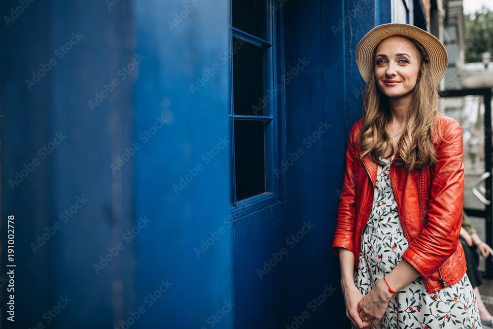 Attractive portrait of a beautiful young girl in a hat, in a red jacket near a blue wall, in a good mood and with a charming smile Attractive portrait of a beautiful young girl in a hat, in a red jacket near a blue wall, in a good mood and with a charming smile