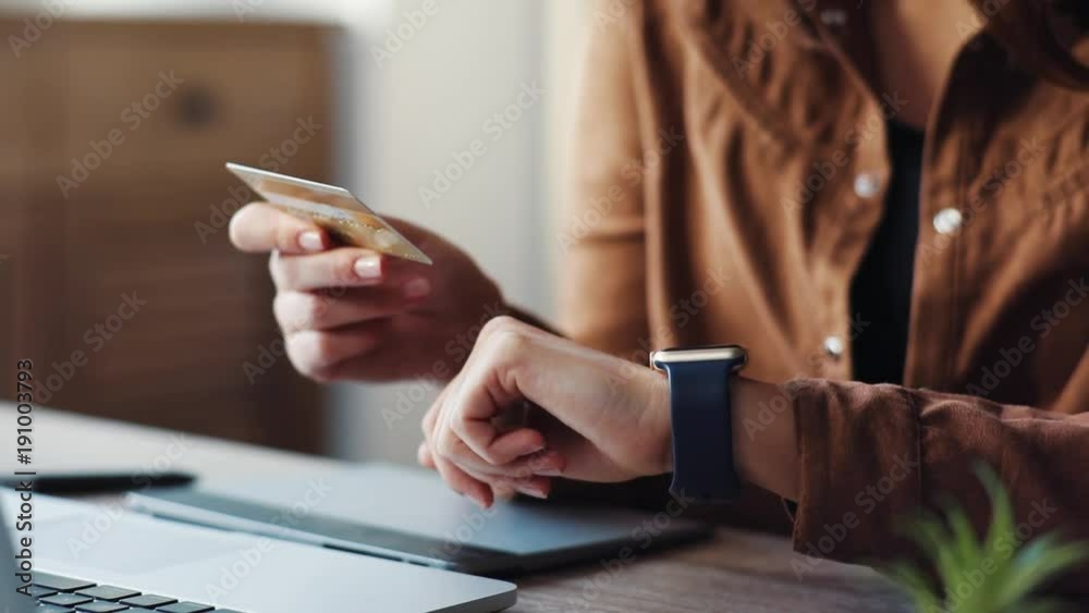 Modern girl holding gold bank card in hands, entering data on screen of smart watch. Young Caucasian woman using new gadget at home. Modern girl holding gold bank card in hands, entering data on screen of smart watch. Young Caucasian woman using new gadget at home.