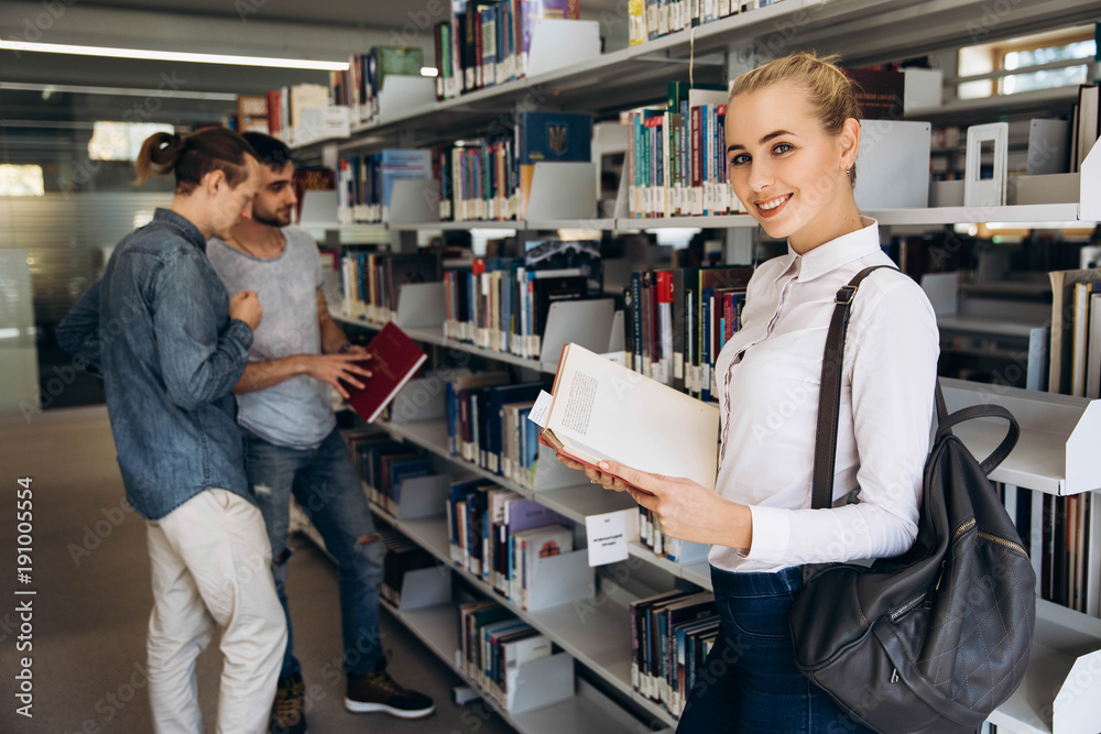 Pretty thoughtful girl looks like student standing with book in the library of a university
