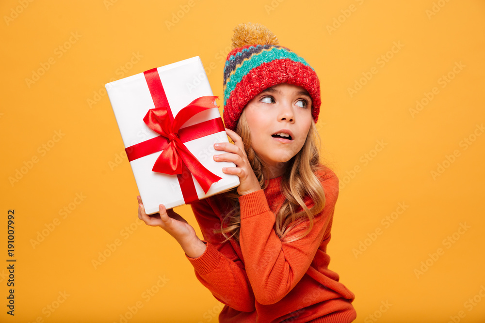 Intrigued Young girl in sweater and hat holding gift box Intrigued Young girl in sweater and hat holding gift box