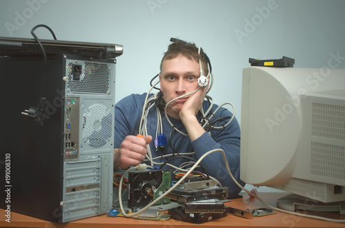 Tired and bored computer repairman is sitting on his workplace and thinking. Computer technician tired from his work and users. PC repair service center.