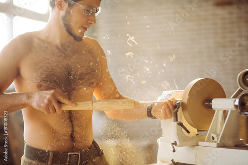 Turner working on a lathe in the workshop. Male hand carved wooden blank photo