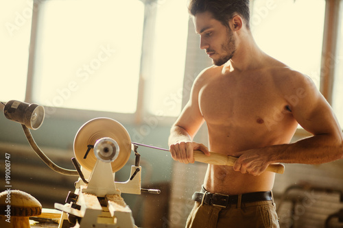 naked man carpentering in workshop and using small manual lathe photo